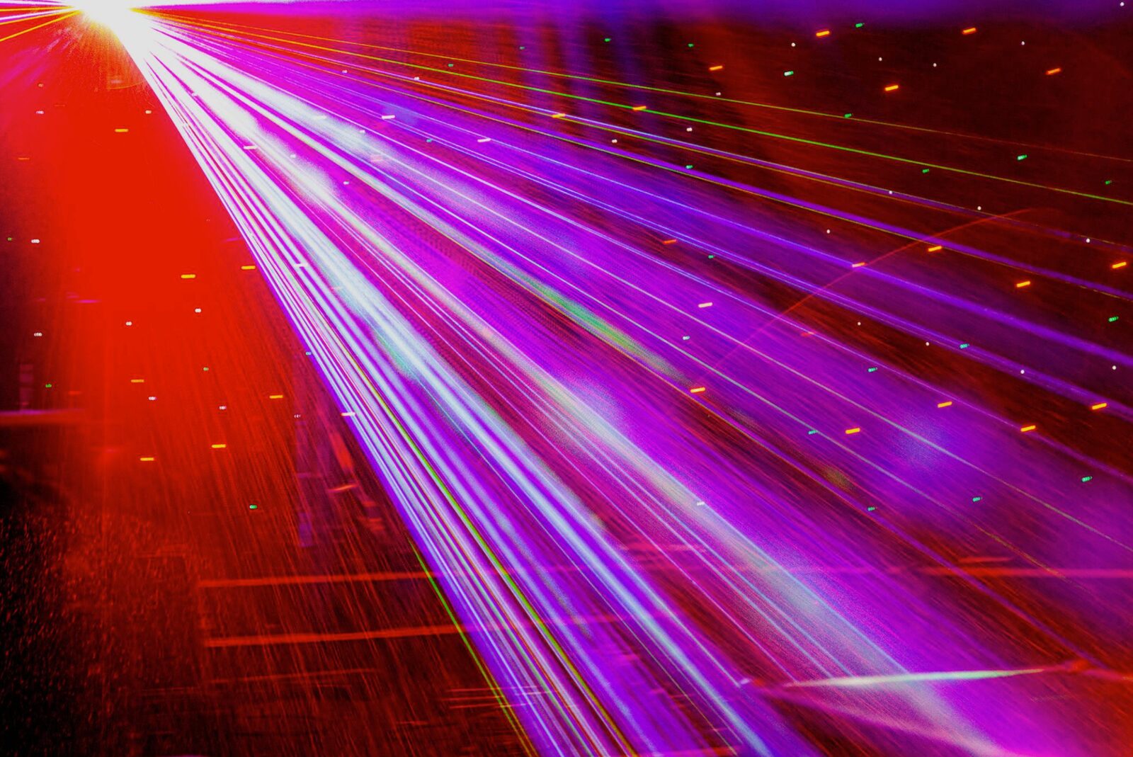 Neon light streaks across a night highway